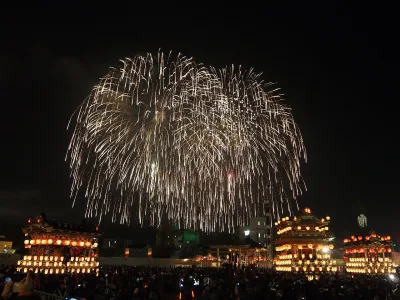 Fireworks burst over a row of lantern-lit festival floats at night during the Chichibu Night Festival