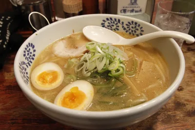 A bowl of ramen in Sapporo with soft-boiled egg halves, green onion and bamboo shoots in a cloudy broth