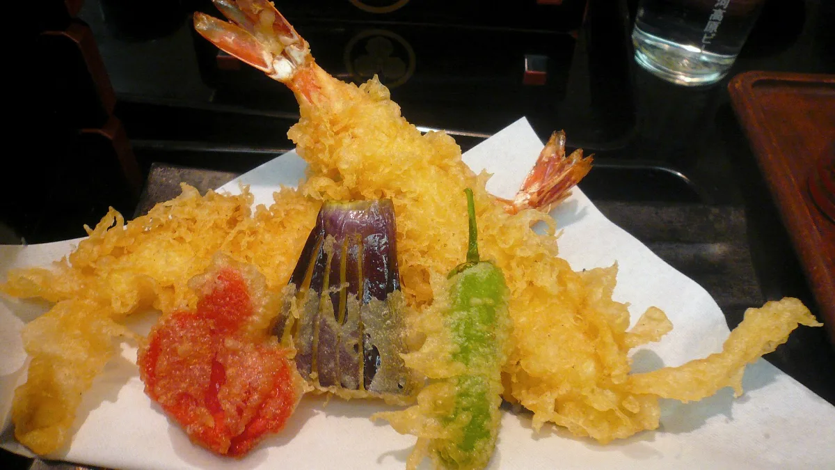 Shrimp and vegetable tempura, including eggplant and green pepper, on paper on a plate