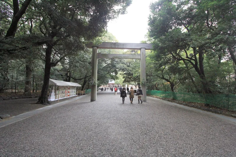 A plain wooden torii gate over the wide gravel approach through the Atsuta Jingu forest