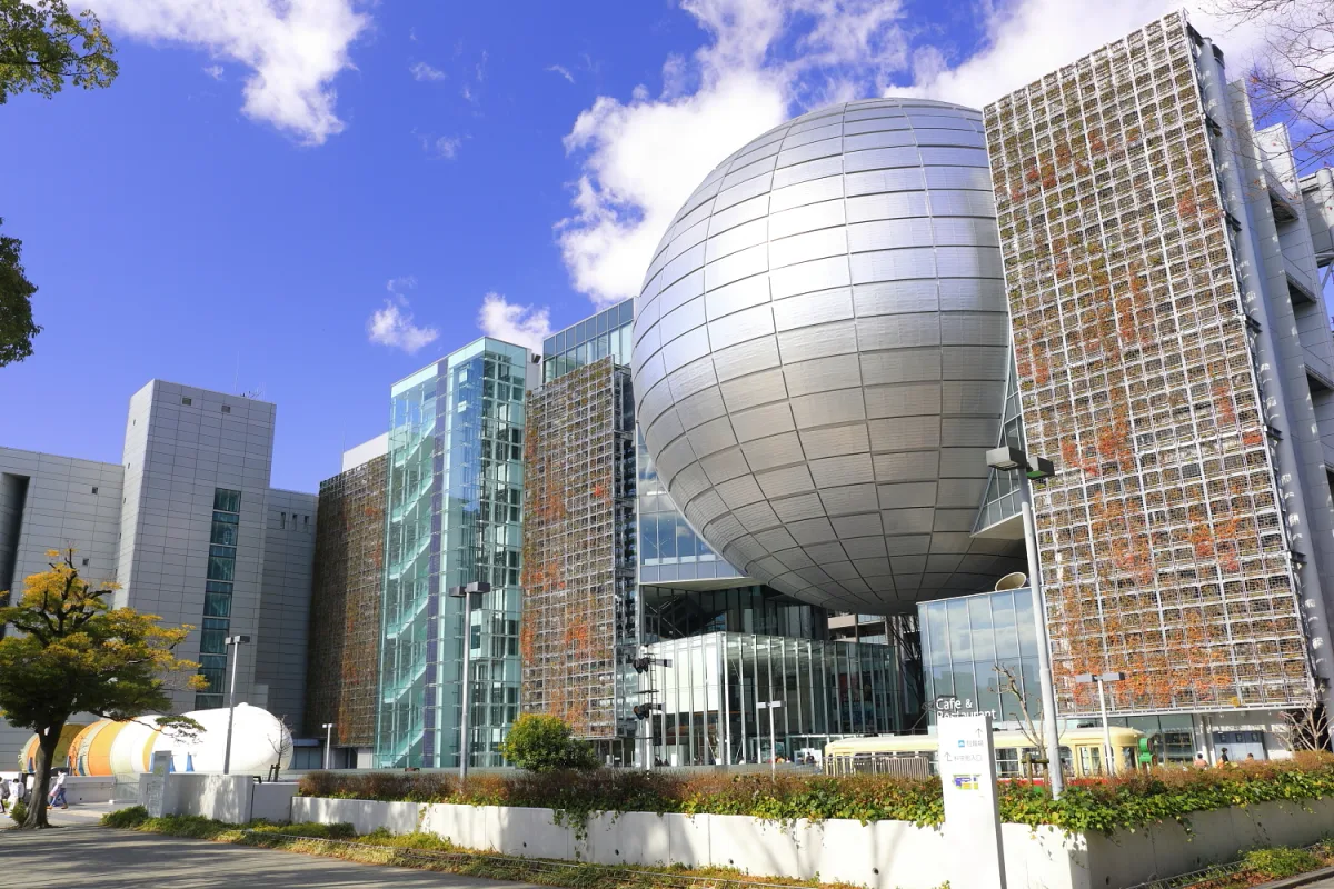 The giant silver planetarium sphere of Nagoya City Science Museum set between glass and green-walled buildings