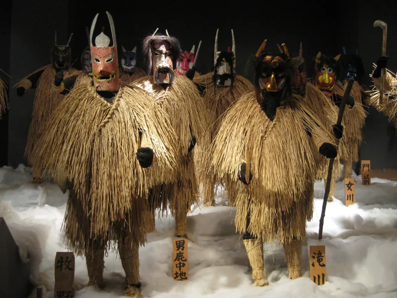 Namahage figures in straw capes and wooden masks standing on fake snow