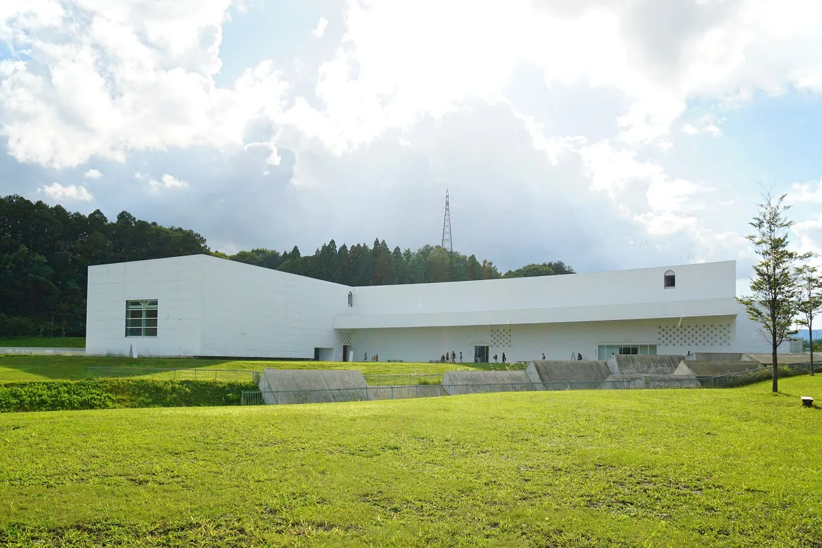 The low white Aomori Museum of Art building beyond a wide green lawn, with forest behind