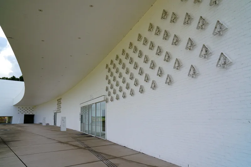 Curved white brick wall of the Aomori Museum of Art with rows of tree-shaped symbol signs