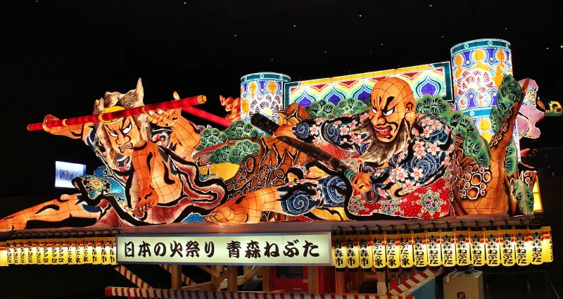 Large illuminated nebuta float of warriors displayed in the dark hall of Wa Rasse