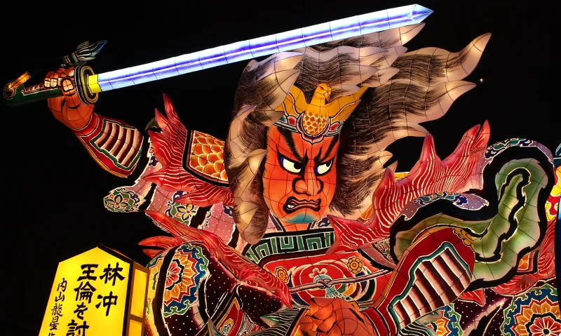 Close-up of a glowing nebuta float showing a fierce warrior holding a sword