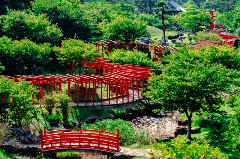 Rows of red torii snaking through green trees and a red bridge at Takayama Inari Shrine