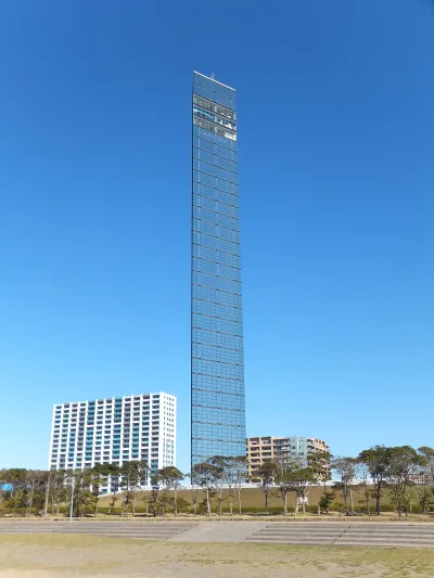 Tall glass-clad Chiba Port Tower reflecting the blue sky, seen from the park lawn