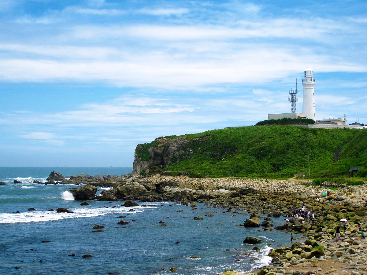 The white Inubosaki Lighthouse on a green clifftop above a rocky Pacific shore