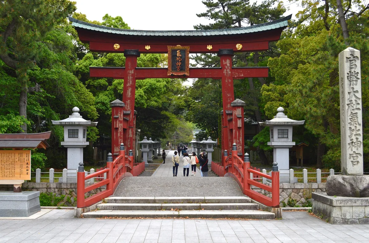 The great vermilion wooden torii gate of Kehi Jingu with stone lanterns and a stone pillar