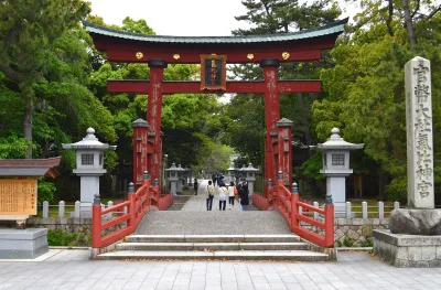 The great vermilion wooden torii gate of Kehi Jingu with stone lanterns and a stone pillar