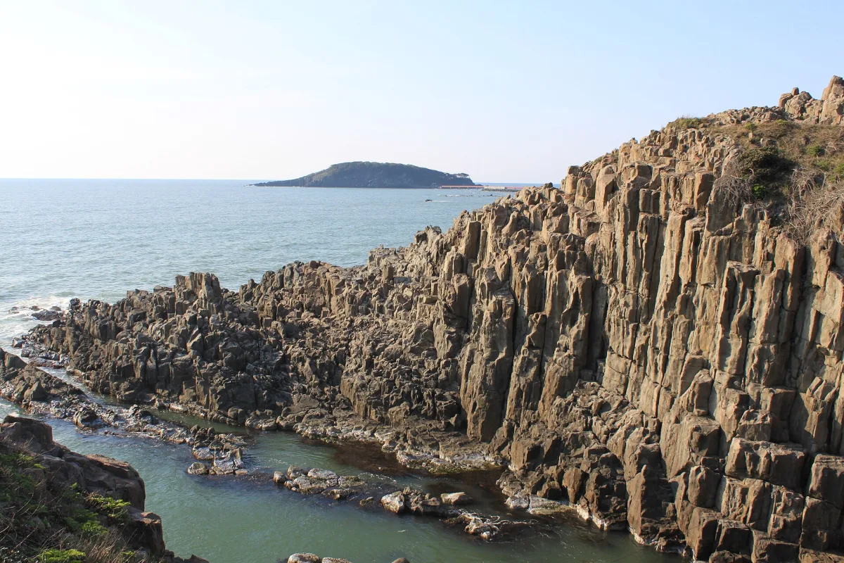 Tall columnar rock cliffs of Tojinbo rising from a sheltered inlet, with an island on the horizon