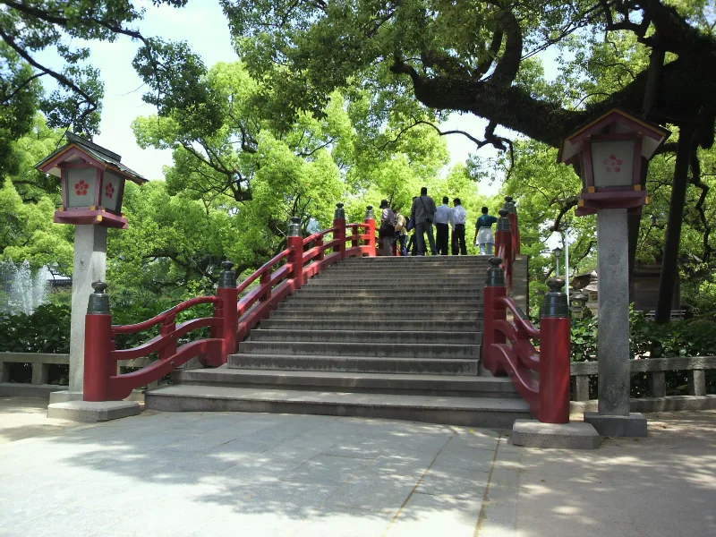 Steep red arched bridge with stone lanterns on the approach to Dazaifu Tenmangu