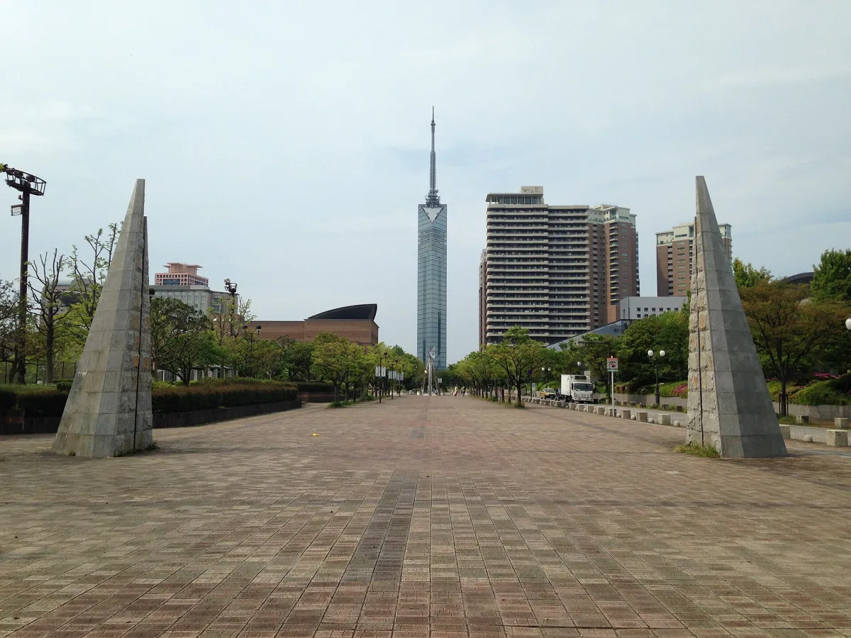 The slim mirrored Fukuoka Tower seen at the end of a wide paved promenade