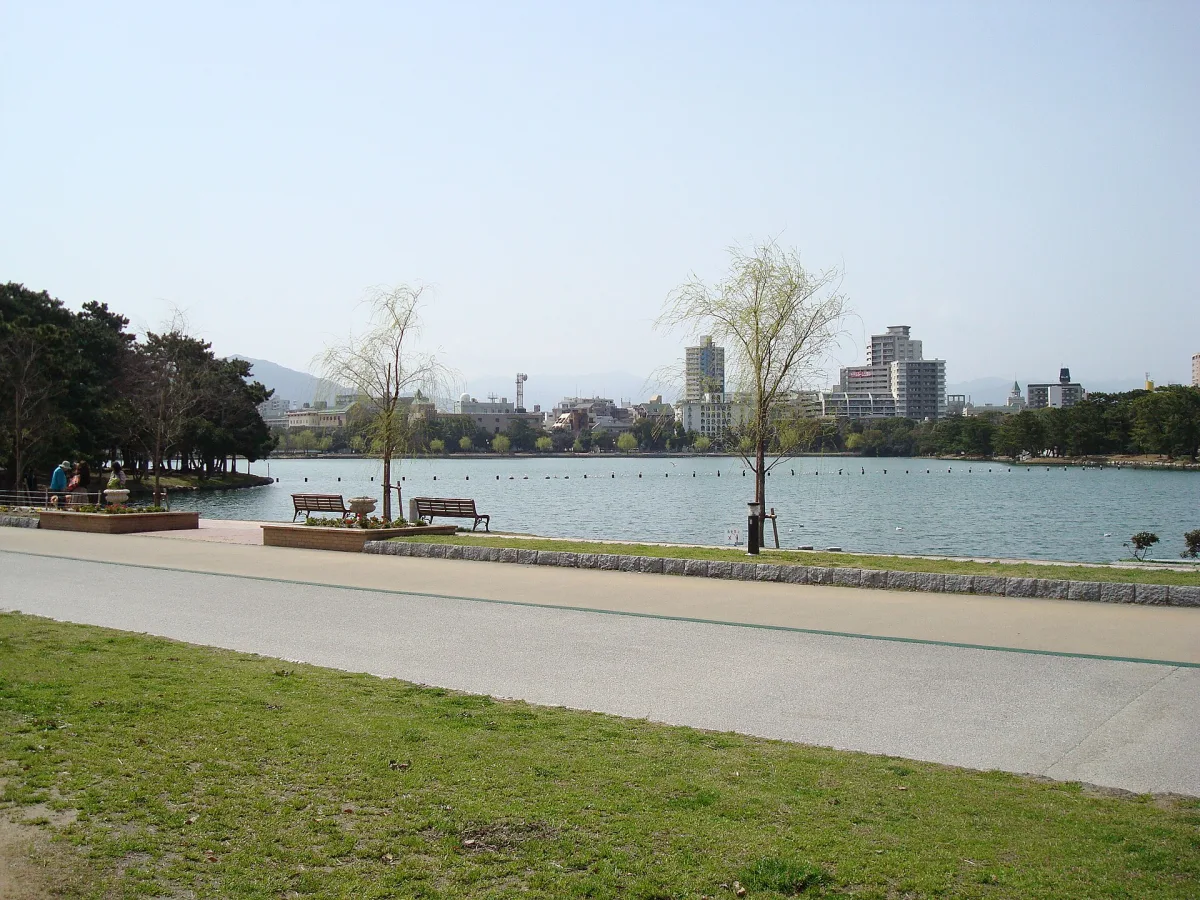 Lakeside path and benches along the wide pond of Ohori Park with Fukuoka buildings beyond