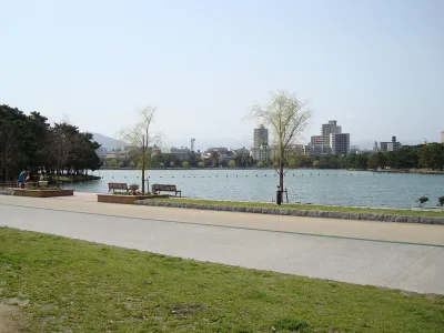 Lakeside path and benches along the wide pond of Ohori Park with Fukuoka buildings beyond