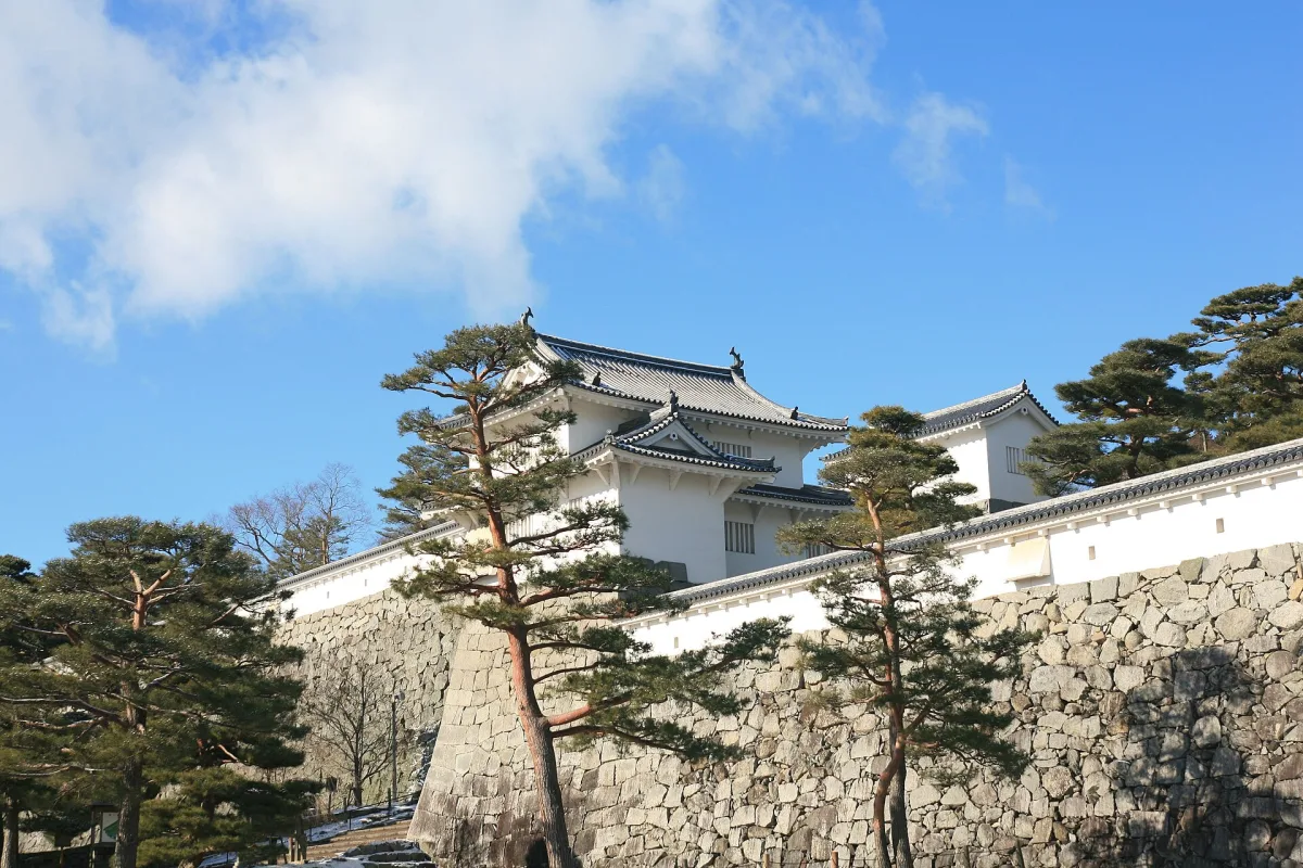 White turret and stone walls of the rebuilt Minowa Gate at Nihonmatsu Castle among pine trees