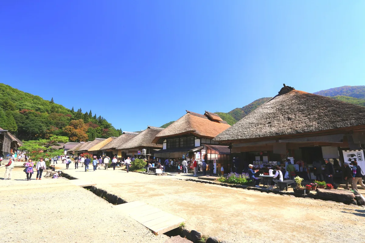 Thatched-roof houses lining the wide main street of Ouchi-juku under a blue sky