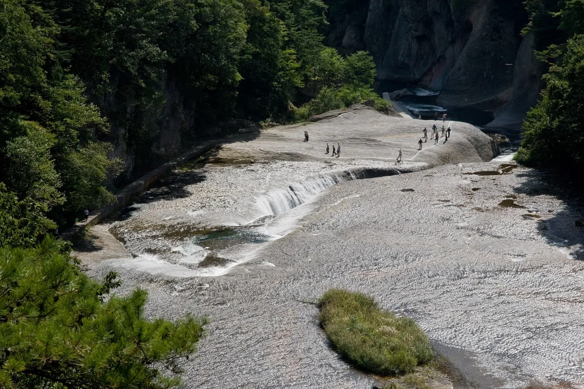 Wide rock riverbed at Fukiware Falls with water pouring into a long crack, visitors walking on the rock