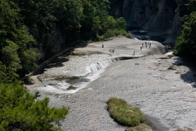Wide rock riverbed at Fukiware Falls with water pouring into a long crack, visitors walking on the rock