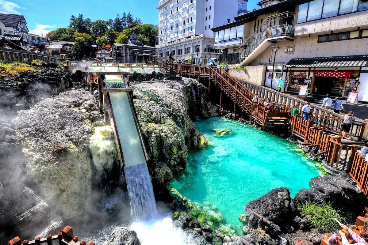 Kusatsu Yubatake with hot water pouring from wooden channels into a turquoise pool, inns around it