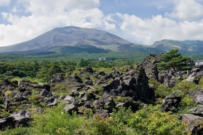 Black lava rocks and green shrubs at Onioshidashi with Mount Asama rising behind
