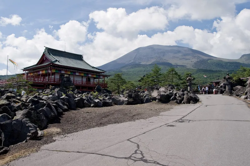 Red Kannon hall among lava rocks at Onioshidashi Park, Mount Asama in the background