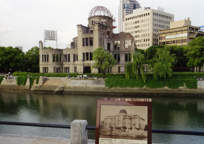 Atomic Bomb Dome across the Motoyasu River, with a sign showing a photo of the building before the bombing