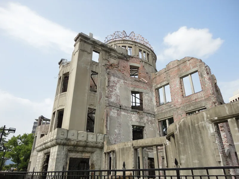 Side view of the Atomic Bomb Dome's damaged walls and steel dome frame behind a fence