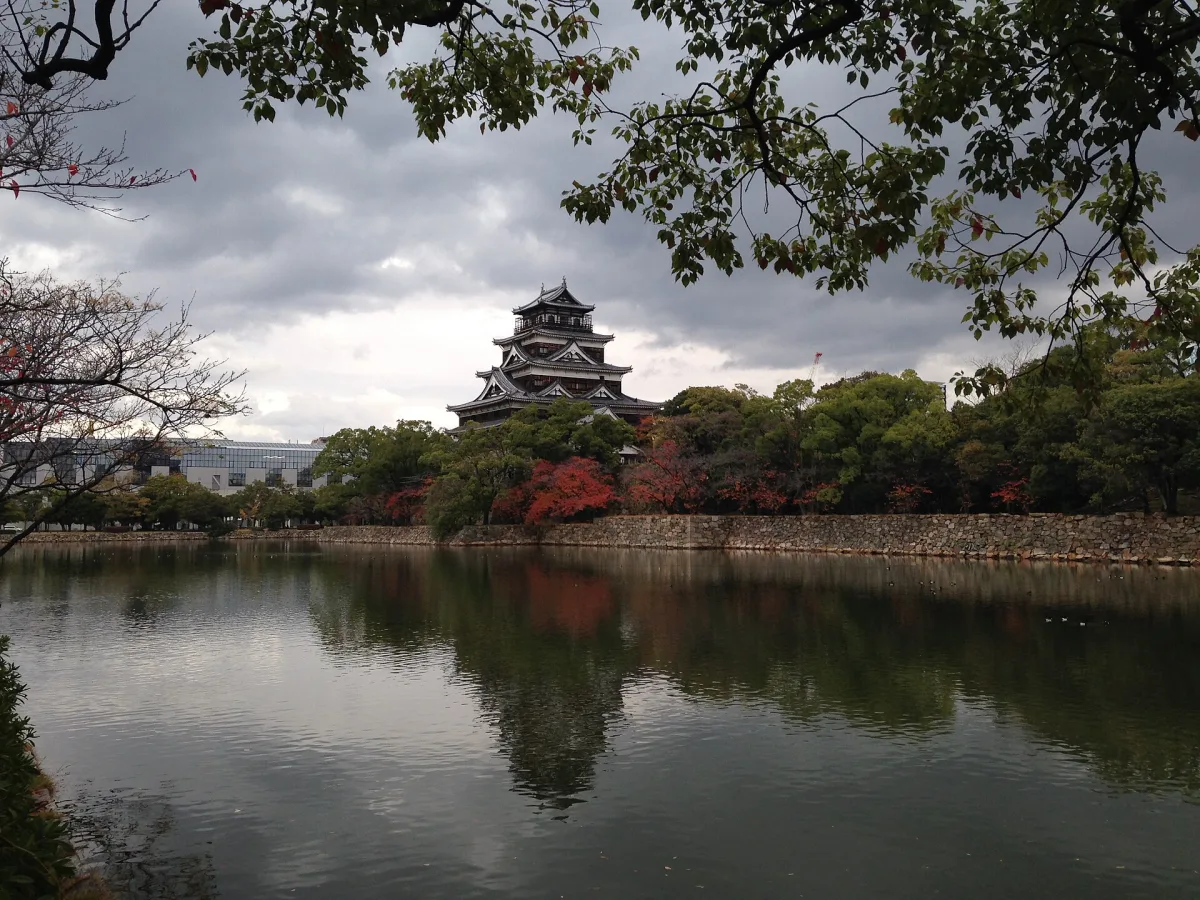 Hiroshima Castle's keep rising above trees and its reflection in the moat