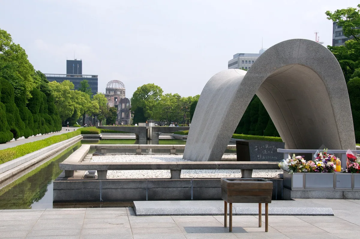 The arched Memorial Cenotaph in Hiroshima Peace Memorial Park, with the A-Bomb Dome visible in the distance