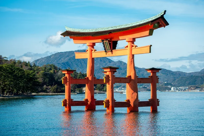 The great vermilion torii of Itsukushima Shrine standing in the sea at high tide, hills behind