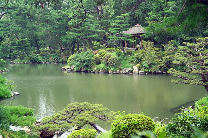 Pond, small islands and a thatched pavilion among trees at Shukkeien Garden