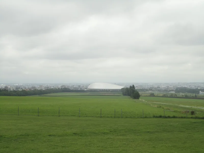Green pasture at Hitsujigaoka with the Sapporo cityscape and a domed stadium in the distance