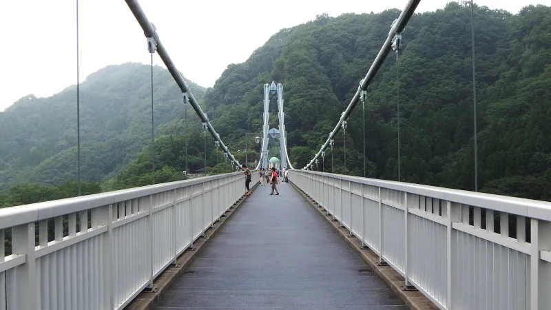 Walkway of the Ryujin Suspension Bridge stretching toward its far tower between green hills