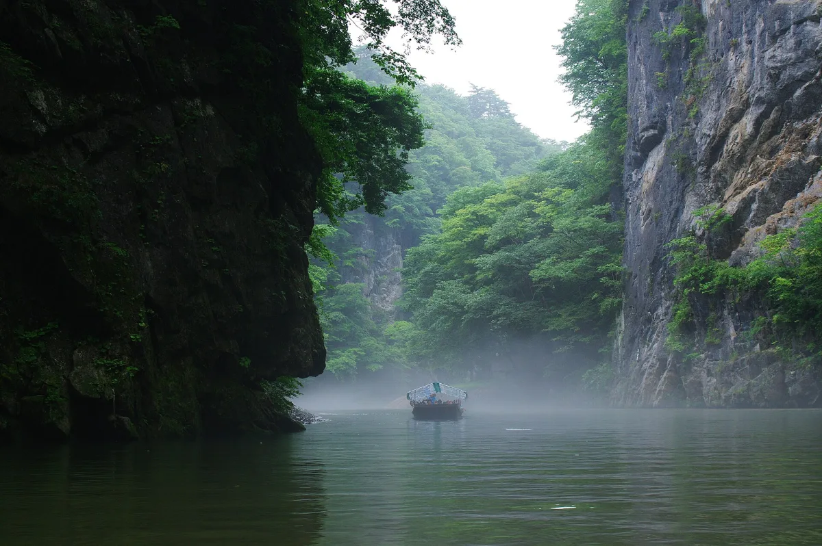 A small boat on the misty green river between tall rock cliffs at Geibikei Gorge