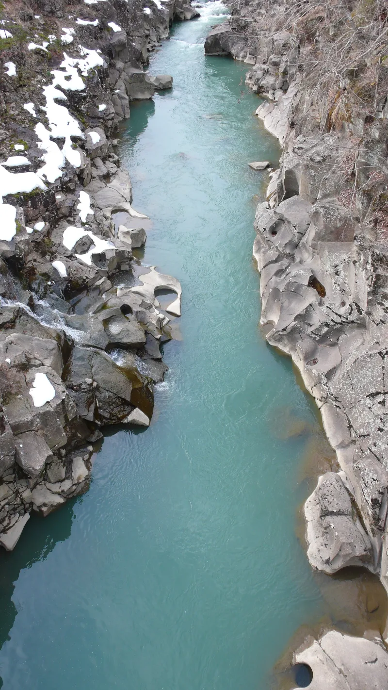 Emerald-green river flowing between smooth, eroded rocks dusted with snow at Genbikei