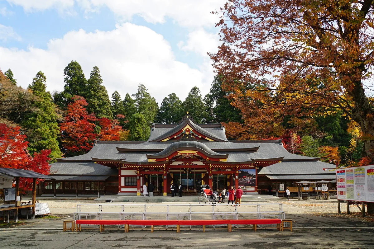 Vermilion main hall of Morioka Hachimangu Shrine with autumn trees and cedars