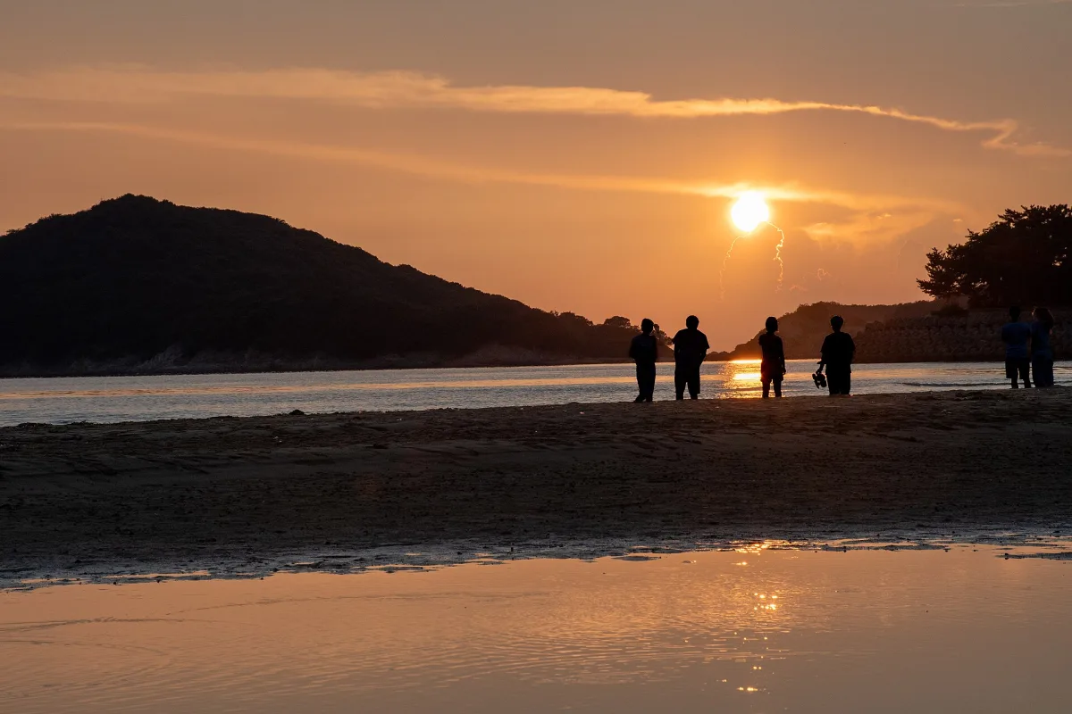Silhouetted people on wet sand at Chichibugahama at sunset, the sky reflected in shallow water