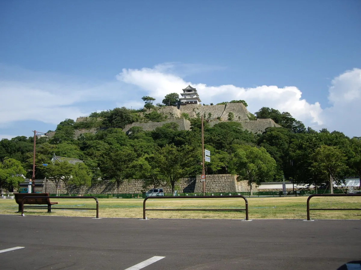 Marugame Castle keep on top of a wooded hill with layered stone walls, seen from the park below