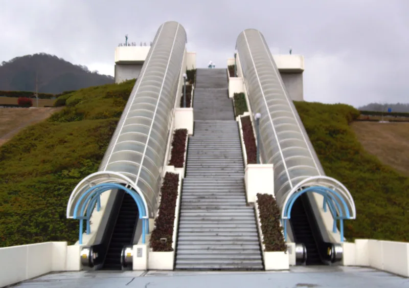 Covered escalators climbing a grassy slope at the entrance of NEW Reoma World