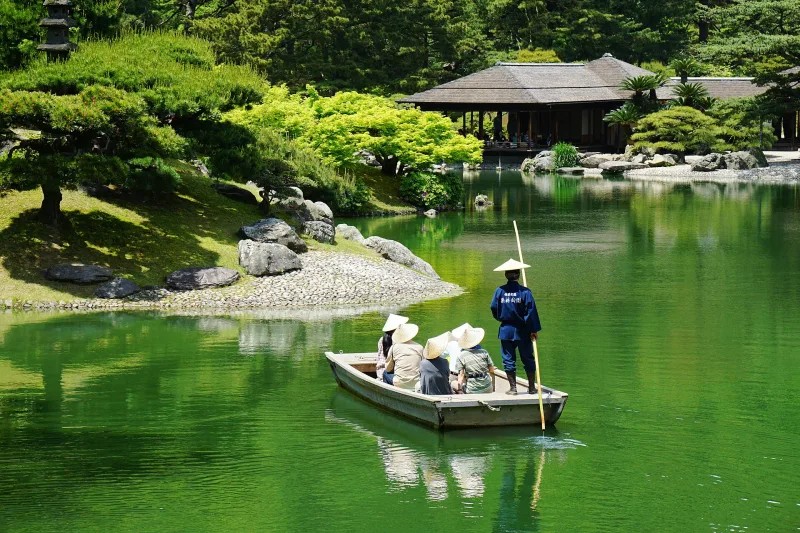 A boatman poling a traditional wooden boat past the teahouse on Ritsurin Garden's South Pond