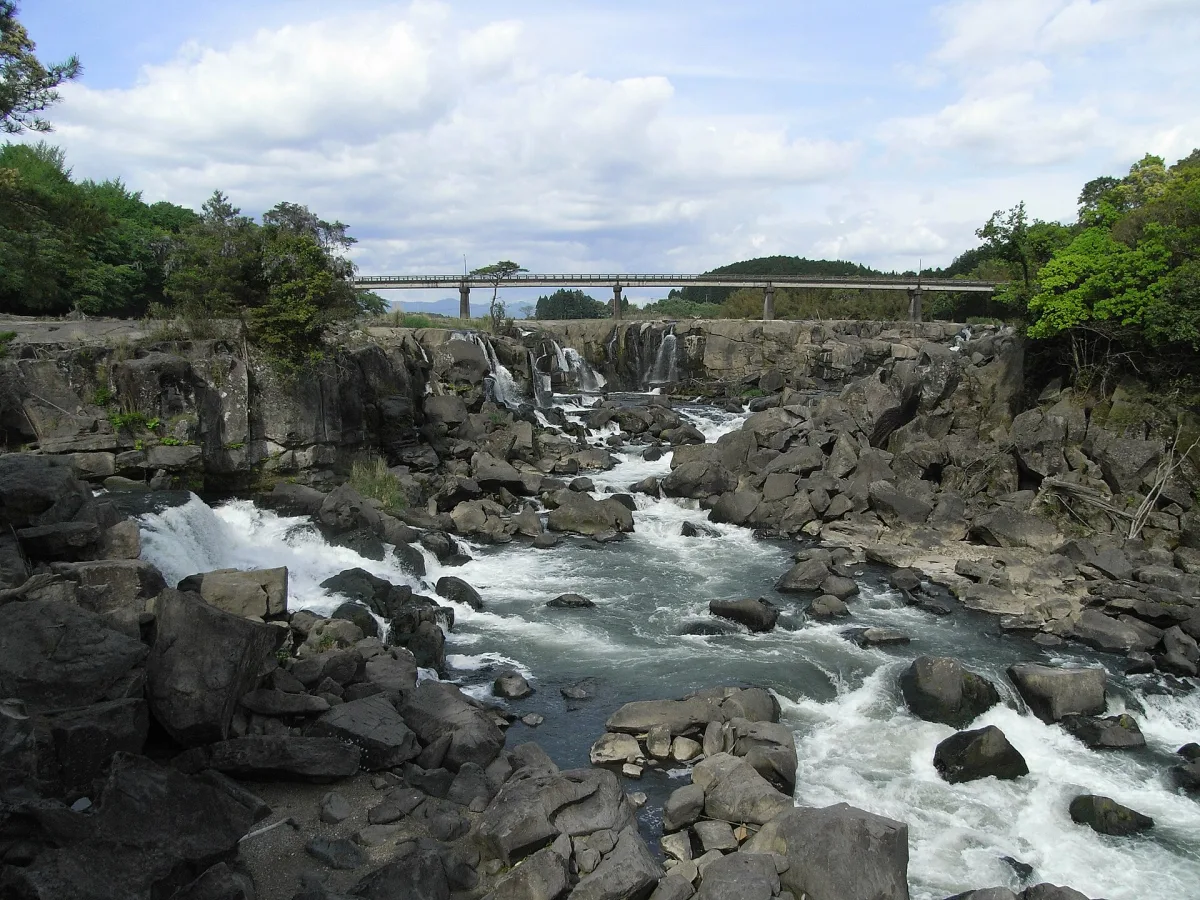 Wide Sogi Falls rushing over dark volcanic rock with a bridge in the background