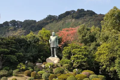 Bronze statue of Saigo Takamori in army uniform standing in a garden with Shiroyama Hill behind