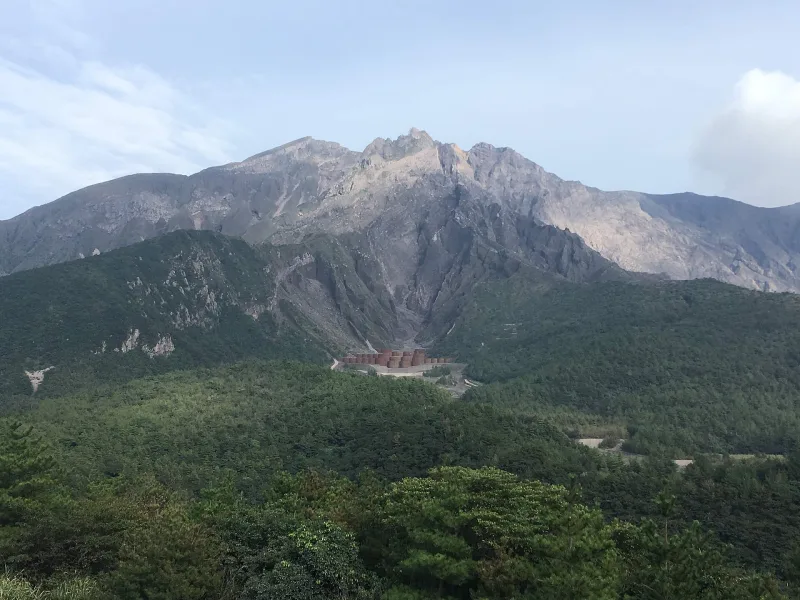The volcanic peaks of Sakurajima rising above green forest, seen from Yunohira Observatory