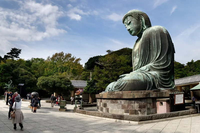 Side view of the Great Buddha of Kamakura with visitors in the temple grounds