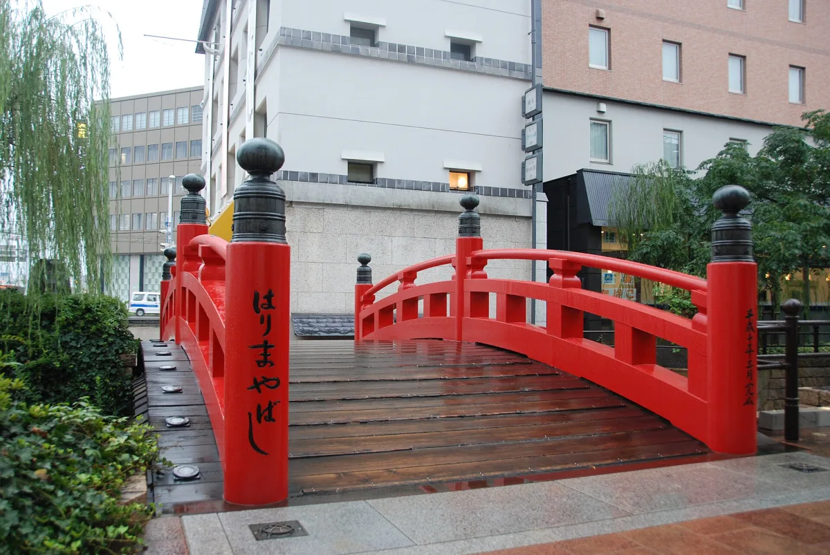 The small red-lacquered Harimaya Bridge with black post caps, surrounded by city buildings