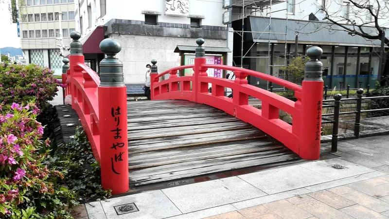Close view of the red wooden Harimaya Bridge with flowering shrubs beside it