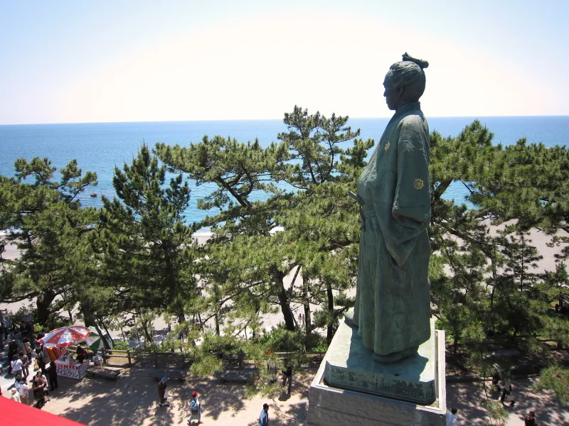 Bronze statue of Sakamoto Ryoma standing above pine trees, looking out to the Pacific Ocean