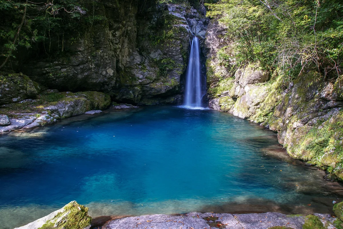 Slender waterfall dropping into the deep blue pool of Nikobuchi in a mossy rock gorge